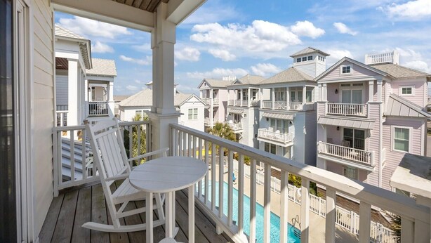 A balcony with a white rocking chair and a small table, overlooking a row of multi-story buildings with balconies. - Seas The Day 3 Bedroom Home by RedAwning (Atlantic Beach)