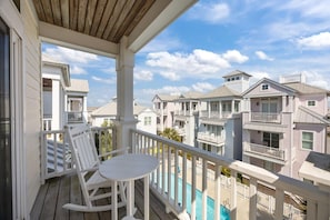 Un balcon avec une chaise berçante blanche et une petite table, donnant sur une rangée d’immeubles à plusieurs étages, chacun doté d’un balcon.
