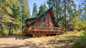 A cabin with a deck, surrounded by tall trees.