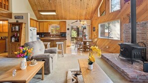 A cabin interior with a wooden ceiling, a kitchen, a dining area, and a fireplace.