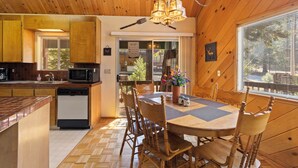 A wooden cabin interior with a kitchen, dining area, and a large window.