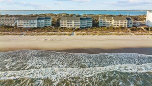 A beachfront hotel with multiple buildings, a sandy beach, and waves in the foreground.