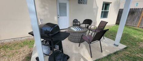Un patio al aire libre con una parrilla, una mesa redonda y cuatro sillas.