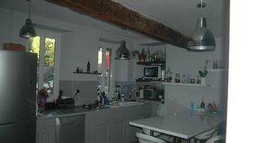 Une cuisine moderne avec des meubles blancs, des appareils en acier inoxydable, un éclairage suspendu et un îlot central doté de tabourets de bar.