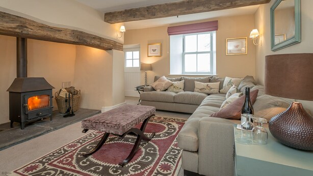 A cozy living room with a fireplace, a sofa, a patterned rug, and a decorative vase. - Luxury Farmhouse in Mountain Location | Cwmain (Corwen)