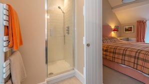 A bedroom with a glass-enclosed shower, a bed with a plaid duvet, and a red lamp on the nightstand. - Luxury Farmhouse in Mountain Location | Cwmain (Corwen)