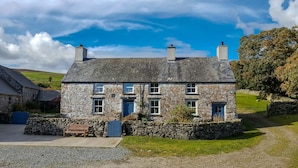 A stone house with a sloped roof, multiple windows, and a stone wall surrounding the property. - Luxury Farmhouse in Mountain Location | Cwmain (Corwen)