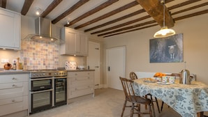 A kitchen with a gas stove, oven, and a dining area with a table set for two. - Luxury Farmhouse in Mountain Location | Cwmain (Corwen)