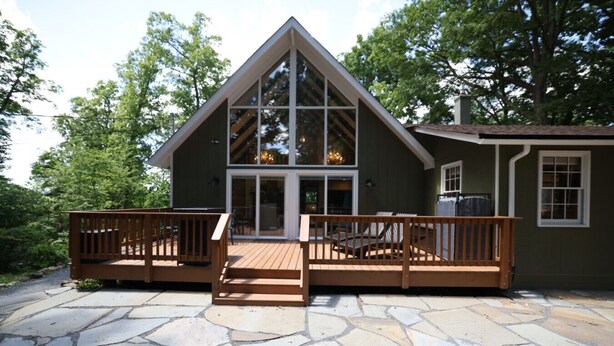 Een chalet met een stenen terras, een houten dek en grote ramen.