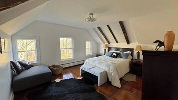 Un dormitorio con techo inclinado, una cama con cubrecama blanco, un sofá gris y un tapete de cuero de vaca negro.