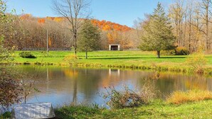 Un paysage paisible avec un étang, des arbres et un petit bâtiment au loin.