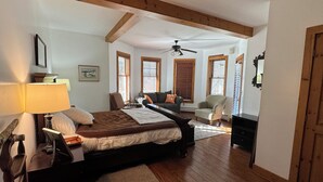 Une chambre à coucher comprenant un lit, une table de chevet, une lampe et une vue sur le salon par une fenêtre.
