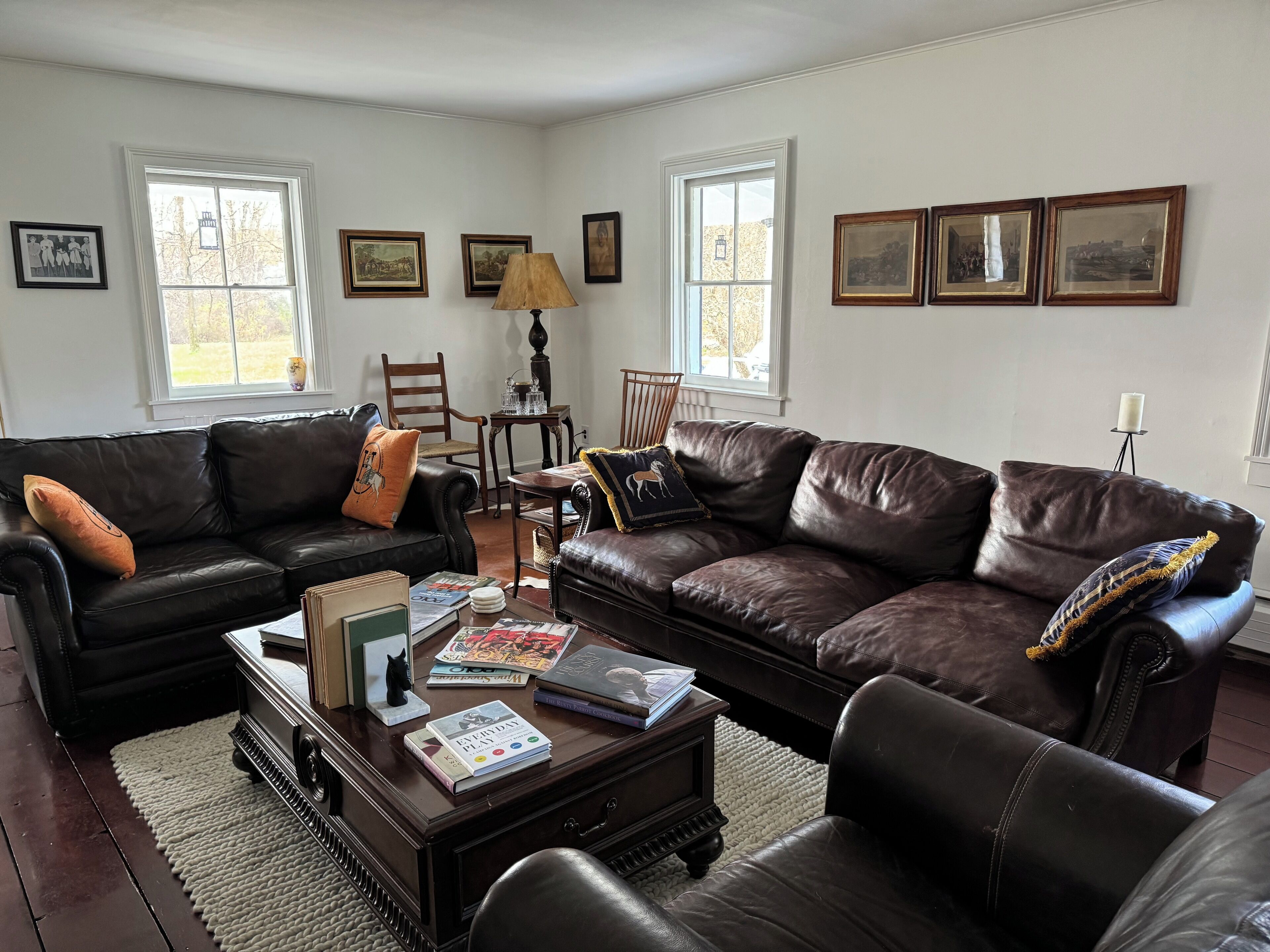 A living room with two leather sofas, a coffee table with books, a lamp, and framed pictures on the walls.