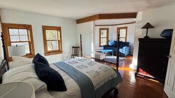 A bedroom with a large bed, a chair, a desk, and a fireplace.