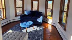 Une pièce d’angle avec un canapé bleu foncé, un pouf gris clair et un tapis à motifs posé sur un plancher en bois.