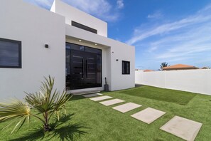 Ein modernes Haus mit weißer Fassade, einer großen schwarzen Garagentür und einem gepflegten Rasen mit trittfesten Steinen.