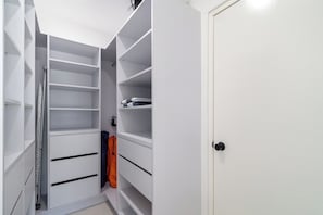 Ein weißer Kleiderschrank mit mehreren Regalen und Schubladen, eine Leiter und eine Tür mit schwarzem Griff.