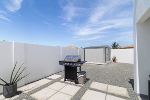 A barbecue grill with a built-in smoker, a small cooler, and a potted plant in a backyard with a white wall and a clear sky. - Aruba Getaway: Luxe Villa, 3BR near Beach (Oranjestad)