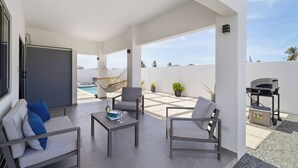 En moderne udendørs terrasse med pooludsigt, siddepladser og grilludstyr.