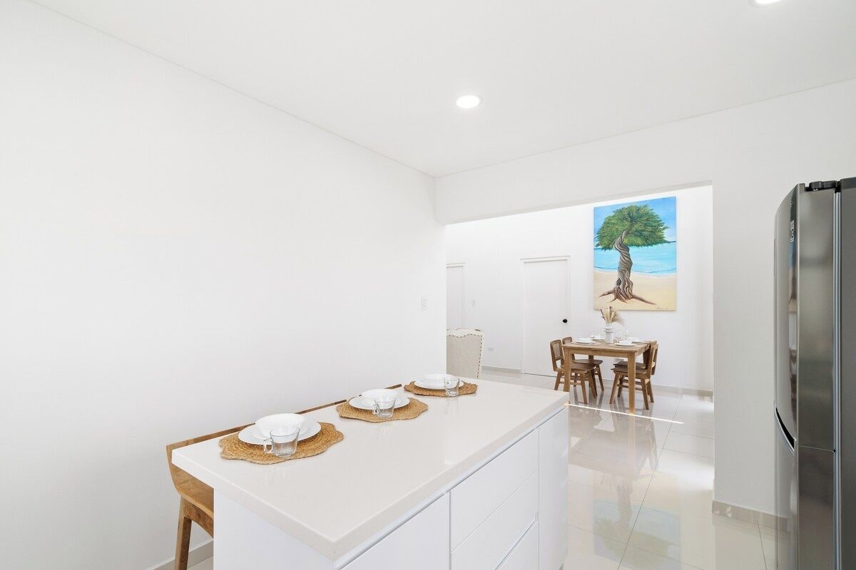 A modern kitchen with a central island, white cabinetry, and a stainless steel refrigerator.