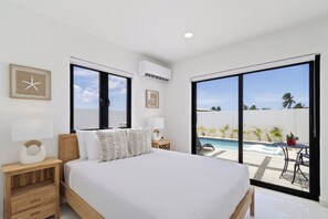 Ein Schlafzimmer mit Bett, Nachttischen, einem Fenster und Blick auf Pool und Außenbereich.