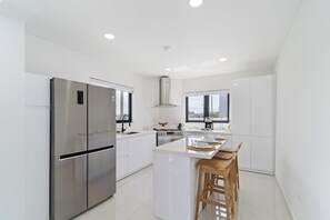 A modern kitchen with stainless steel appliances, a central island with stools, and a large window providing natural light. - Aruba Getaway: Luxe Villa, 3BR near Beach (Oranjestad)