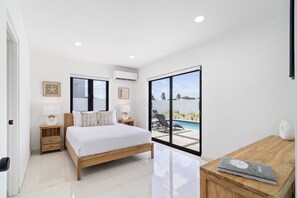 A bedroom with a bed, bedside tables, a lamp, and a view of a swimming pool.