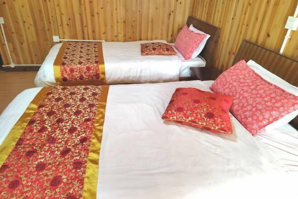 A room with two beds, each with a white bedspread and red floral pillows.