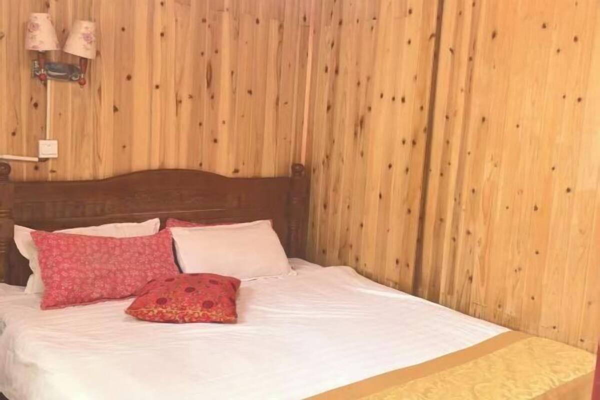 A wooden-paneled room with a bed, pillows, and a wall-mounted lamp.