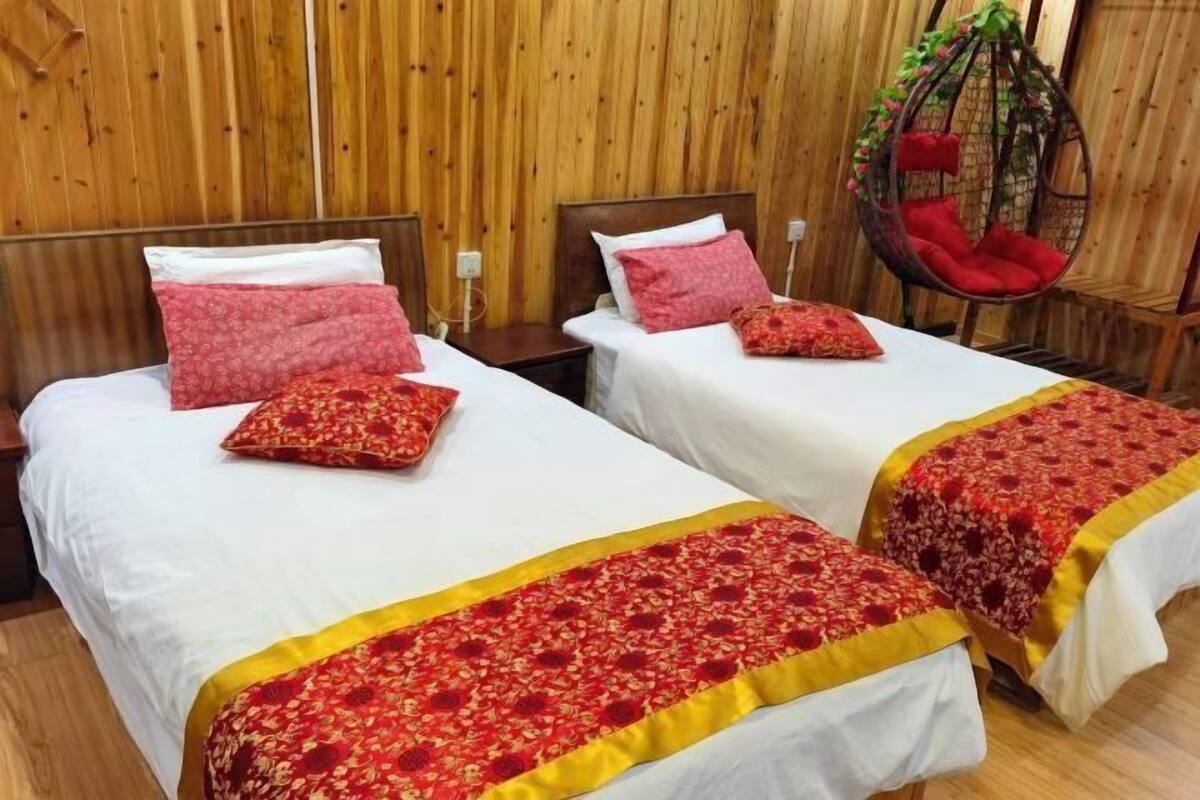 A room with two beds, each with white bedding and red floral bedspreads. There is a hanging chair with red cushions and a wooden wall.