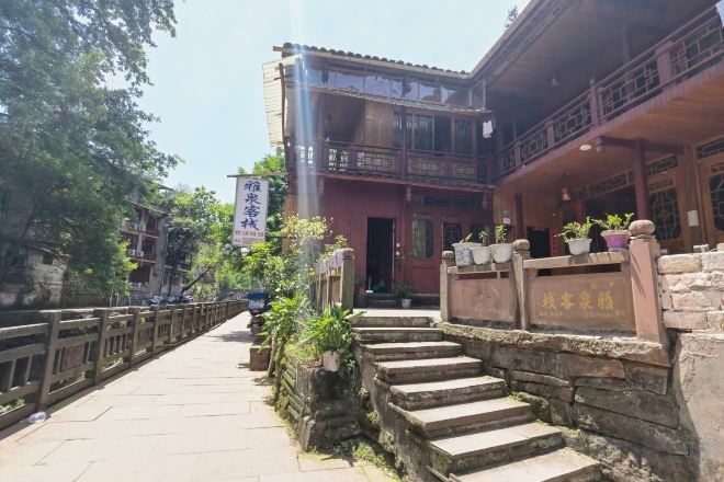 A traditional building with a stone staircase leading to a wooden door, surrounded by greenery and a stone railing.