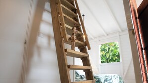 Una escalera de madera en una habitación con paredes blancas y una ventana con vistas a follaje.