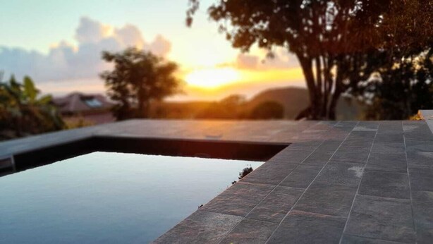 Piscina con borde de piedra, rodeada de árboles y vista al atardecer.