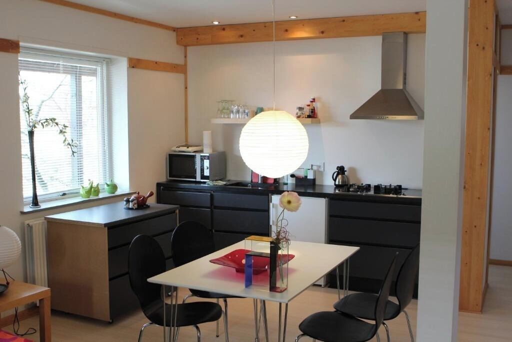 Una cocina moderna con comedor, que incluye una mesa blanca, sillas negras y una lámpara circular grande.
