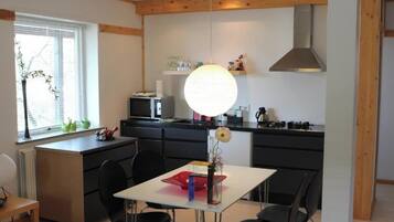 Una cocina moderna con comedor, que incluye una mesa blanca, sillas negras y una lámpara circular grande.