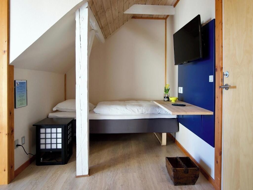 A small, compact room with a single bed, a TV mounted on the wall, and a wooden ceiling.