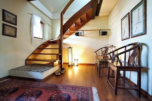 Un loft espacioso con escalera de madera, un pequeño rincón de descanso y un gran ventanal.