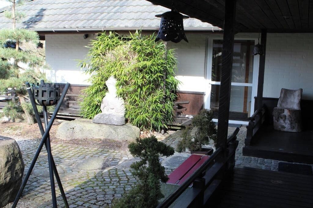Una casa tradicional japonesa con un sendero de piedra, una planta de bambú y una terraza de madera.
