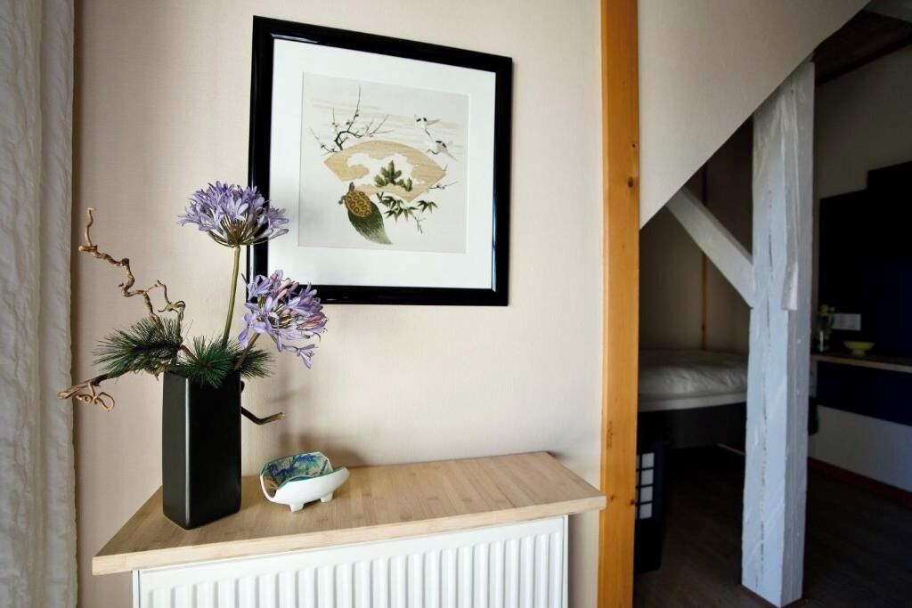 A framed artwork on a wall, a small vase with flowers, and a white radiator below.