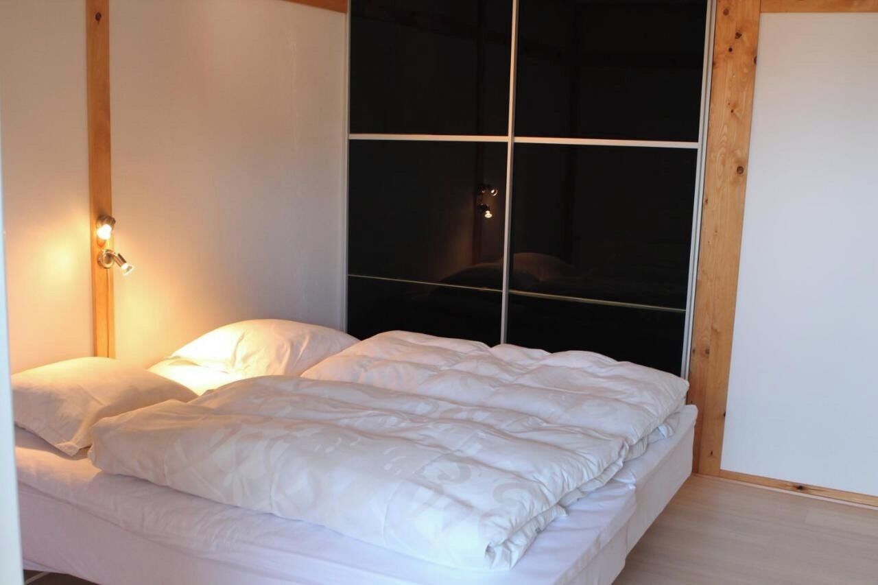 A bedroom with a large window, a bed with white bedding, and a wooden headboard.