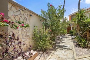 A stone pathway leading to a building with a stone wall and a variety of plants.