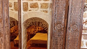 A stone-walled room with a bed, a wooden cabinet with intricate carvings, and a mirror reflecting the room. - Rumet Paşa Konağı (Mardin)