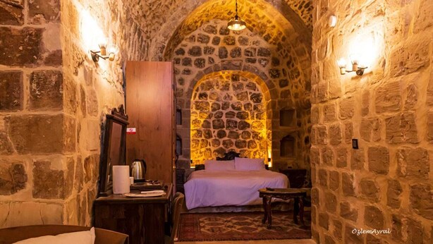 A stone-walled room with a bed, a wooden cabinet, and a small table. - Rumet Paşa Konağı (Mardin)