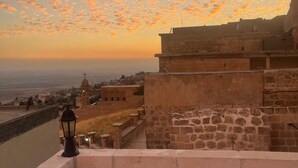A stone fortification with a view of a cityscape and river at sunset. - Rumet Paşa Konağı (Mardin)