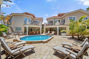 A two-story building with a swimming pool, outdoor seating, and palm trees.