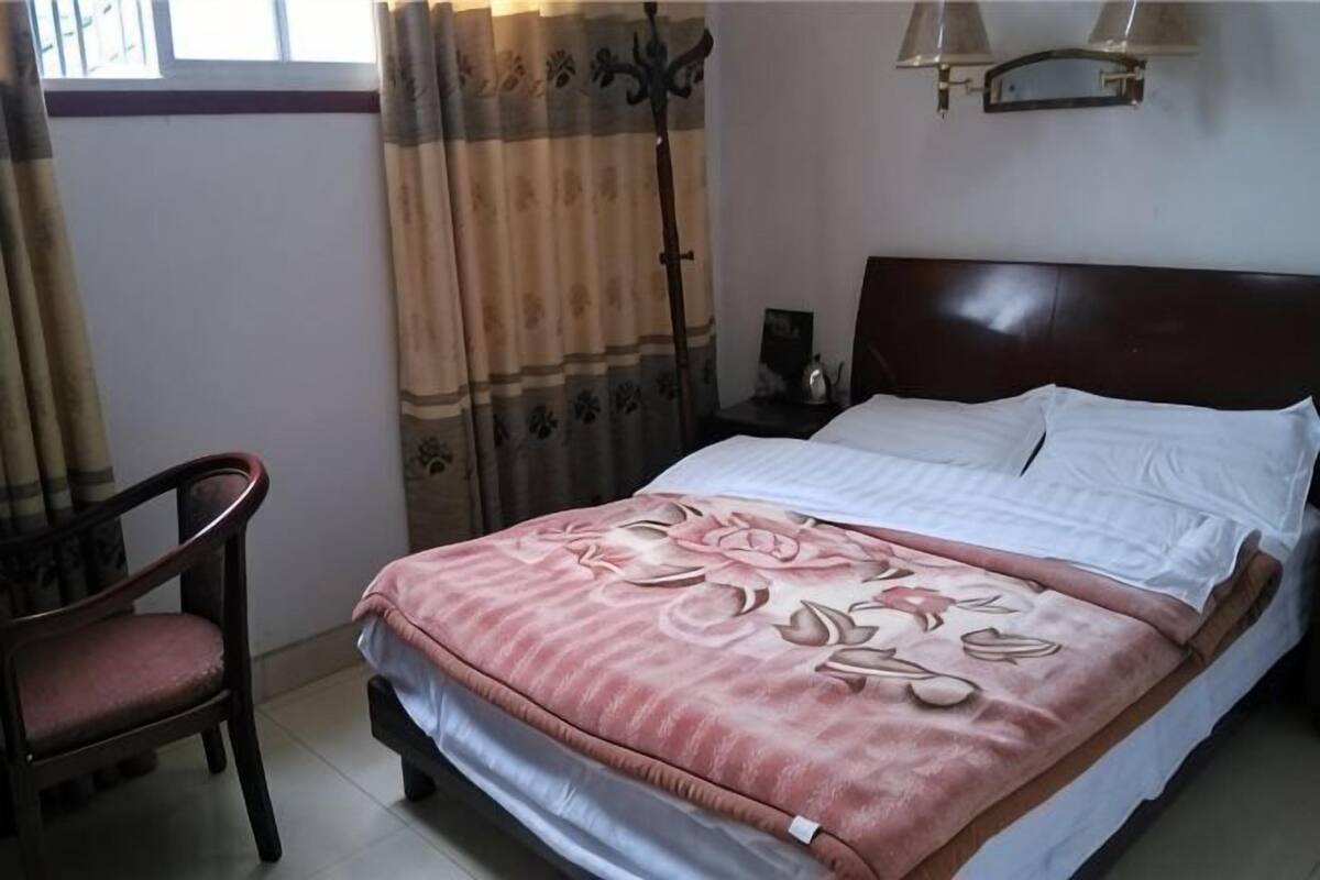 A neatly made bed with a floral bedspread, a wooden nightstand with a lamp, and a chair in a hotel room.