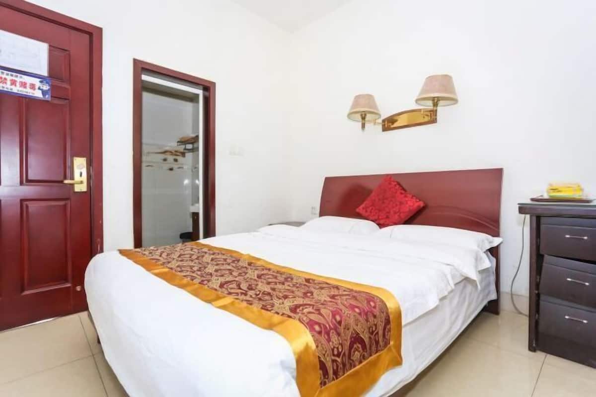 A hotel room with a bed, a wardrobe, a door, and a wall-mounted lamp.