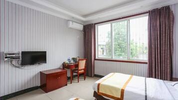 A hotel room with a bed, a desk, a chair, a television, and a window with curtains.