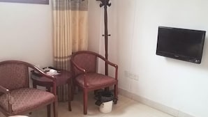 A room with a bed, a TV mounted on the wall, two chairs, a small table, a coat rack, and a window with curtains. - Xinping Hotel (Dayi)