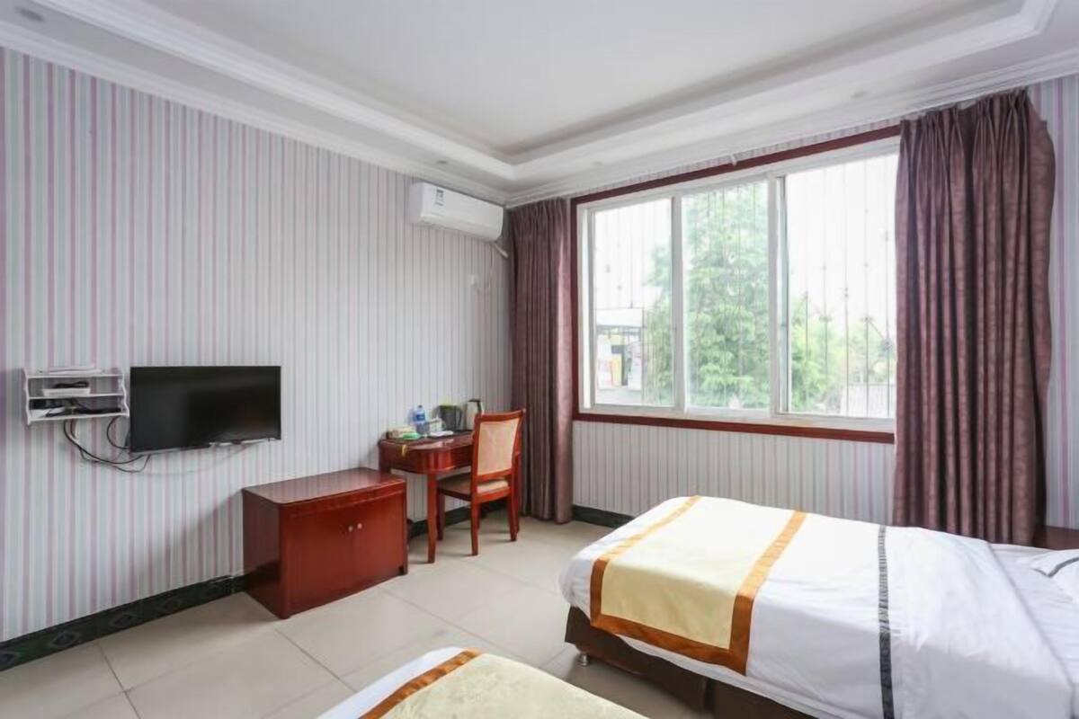 A hotel room with a bed, a desk with a chair, a television, and a window with curtains.